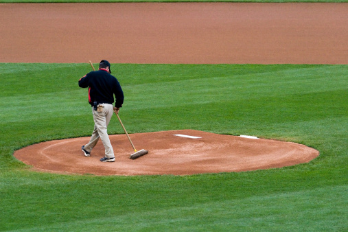 A groundskeeper is preparing the pitcher's mound before a baseball game.