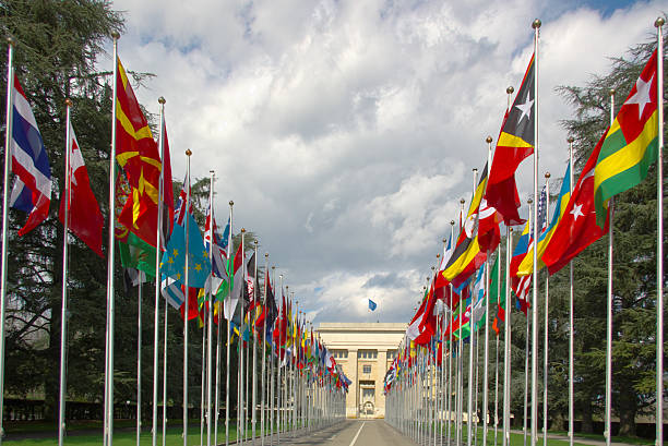 National flags gallery at the entrance to UN perspective view on an avenue with many national flags at the entrance to the UN, Geneva, Switzerland, under stormy clouds. diplomacy stock pictures, royalty-free photos & images
