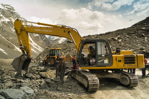 An earth mover with a mechanised shovel and a bulldozer clear a path in a high altitude location where a stream has washed away the unpaved road after excessive rains stock photo