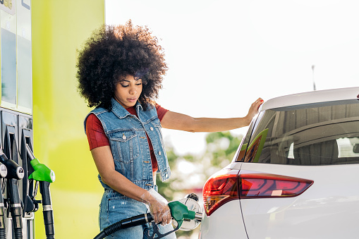 Beautiful woman with afro hair filling her car with gasoline at the gas station.