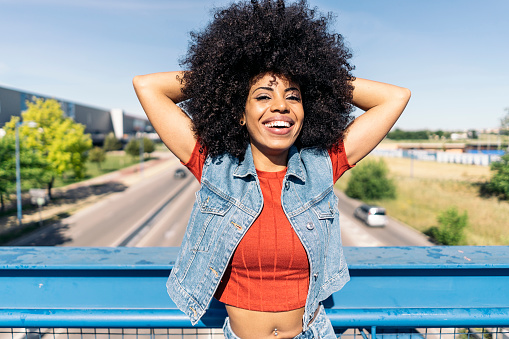 Cheerful black woman with cool afro hair smiling and looking at camera in the city.