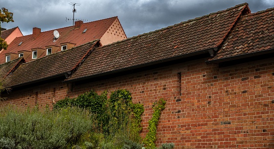 The brick houses with weathered dark brown roofs and green trees under dark cloudy sky in Nuremberg, Germany