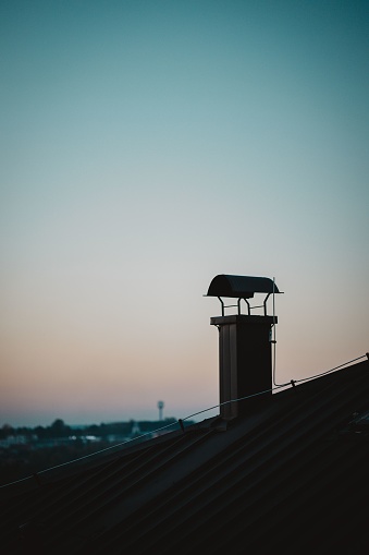 A vertical shot of a chimney on a roof with a blurred view of a late sunset sky