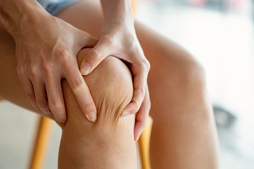 Mujer asiática masajeando su rodilla, sufriendo de dolor en la pierna de cerca photo