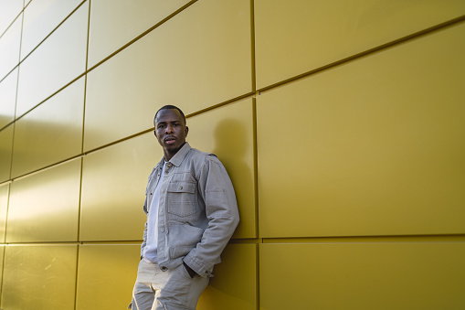A closeup shot of a young Black male standing in front of a yellow wall
