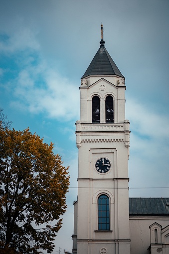 A vertical shot of a clock tower of an old church in daylight in cloudy sky background