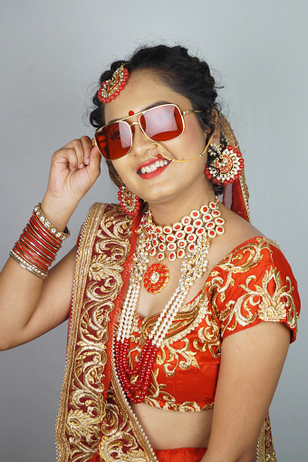 A gorgeous Indian bride with heavy makeup wearing traditional Indian bridal attire and sunglasses
