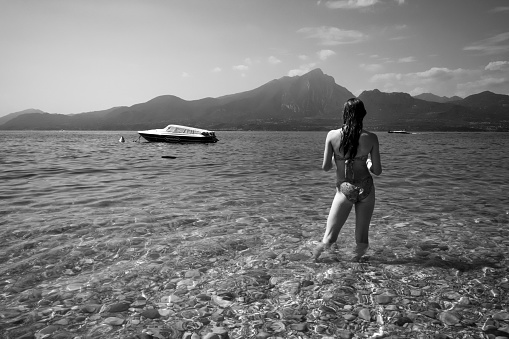 Garda, Germany – August 12, 2019: rear view of young woman standing in water against mountain range