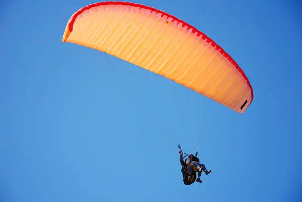 Photo of tandem paraglider, orange parachute and clear blue sky