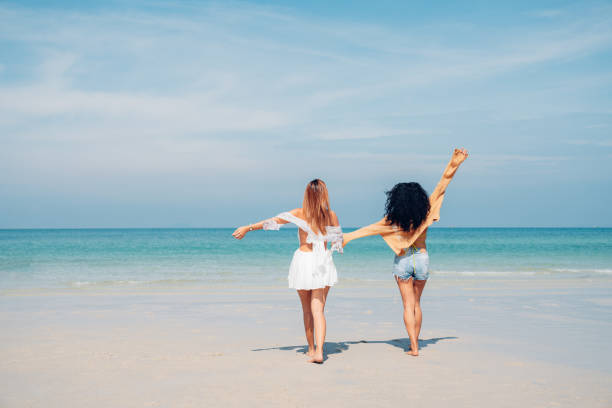 Happy Couple woman walking and dancing together on the beach having fun in a sunny day stock photo