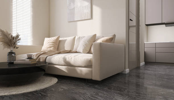 istock Cream colored sofa with cushion and round black coffee table in luxury white wall and marble floor living room with sunlight from window blinds connected to kitchen 1442113522
