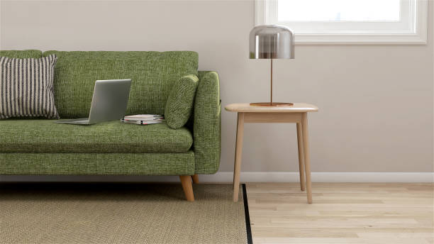 диван из зеленой ткани, деревянный тумбочку с настольной лампой в современном и роскошном и уютном кремовом цвете стены и паркетный пол с к� - side table стоковые фото и изображения