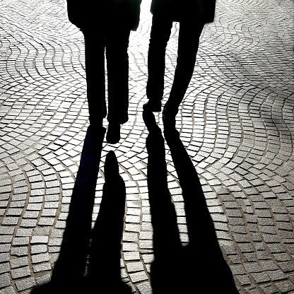A greyscale shot of the shadows of two people's shadow walking on the street
