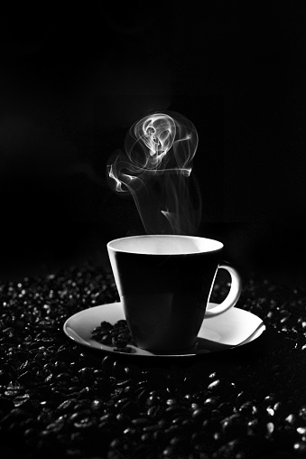 A cup of hot coffee and scattered coffee beans in the black background