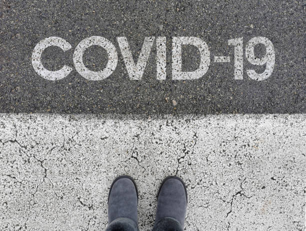 istock Covid-19 text painted on road, asphalt. Personal perspective, feet, standing. 1442116894