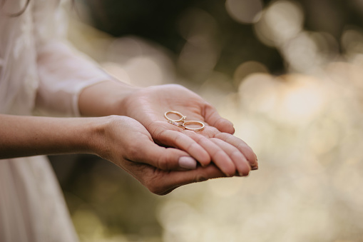 The bride holding the wedding rings in her palm with a bokeh background