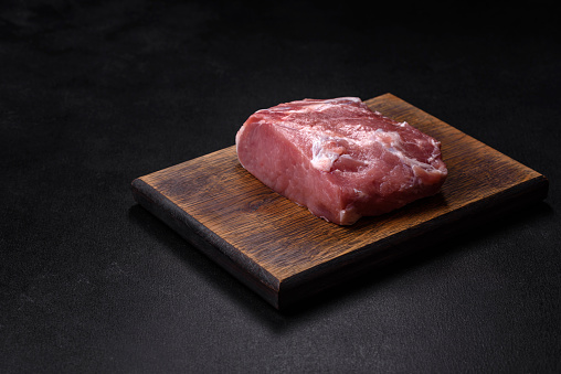 Fresh piece of raw pork with spices, salt and herbs on a wooden cutting board. Cooking grilled meals at home