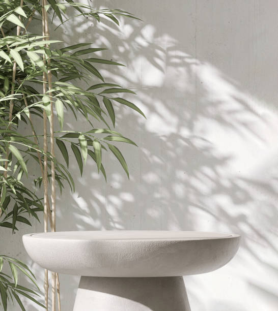 istock Modern, minimal round concrete pedestal table podium with Asian bamboo in dappled sunlight and leaf shadow on white cement wall 1442117501