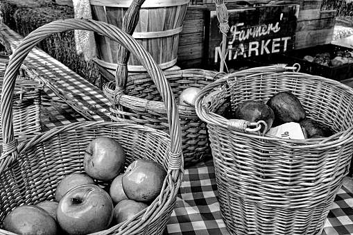 A monochrome closeup shot of baskets filled with big sweet apples in the farmer's market