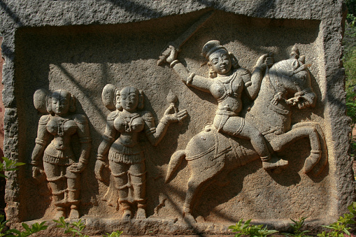 A closeup shot of  an ancient sculpture of three ritual women, one of them is riding a horse with a sword in his hand