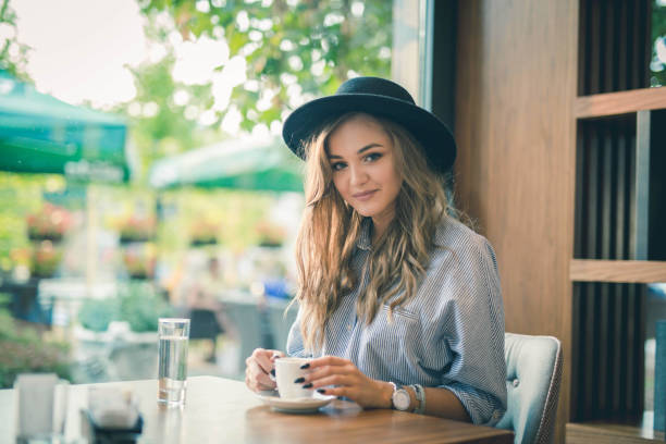 istock Young beautiful female in a hat enjoying a coffee at a cafe 1442120594