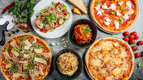 A top view of different types of pizza with pasta and vegetables on a granite table