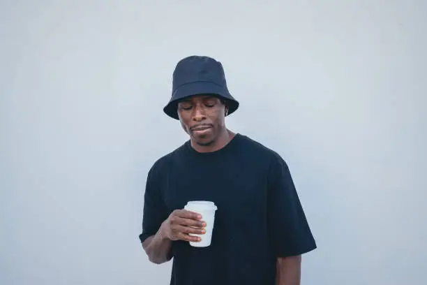 A young black man in street-style clothes holding his takeaway drink on a white background