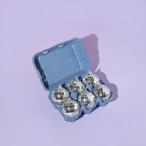 Christmas creative layout with disco ball Christmas baubles in egg box on pastel purple background. 80s or 90s aesthetic fashion party concept. Minimal New Year decoration  idea.