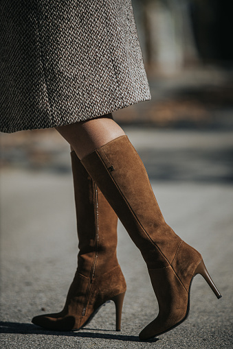 A vertical shot of woman wearing fashionable brown suede knee-high boots outdoors