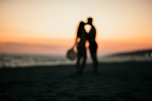 A blurred shot of a romantic couple kissing silhouette on a beach with background of a beautiful sunset.