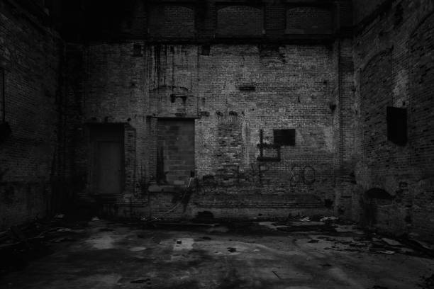 A grayscale view of an old rusty black wall with little shadows with an old broken ground, creepy view