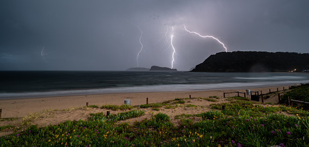 A panoramic shot of a beach surrounded by the sea and hills during the lightning in the evening