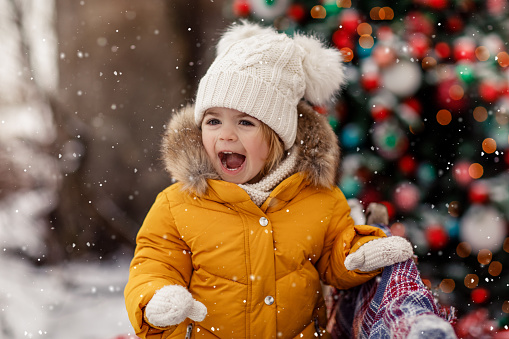 Child playing snowy outdoor wear colorful winter outerwear. Christmas and New Year tree cosy background. Concept of childhood and happiness. Cute children playing with snow outdoor. Holidays winter season.