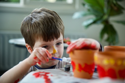 Toddler painting clay pots concentrating and focussing on paint with messy hands
