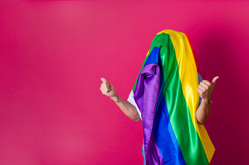 Unrecognizable person with LGBT flag covering his head. Gay pride concept. Fuchsia background with copy space.