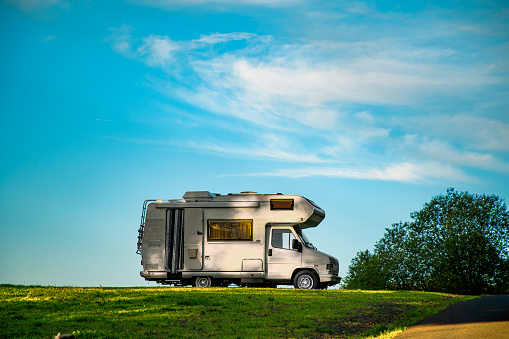 A closeup shot of a camper van parked in the green field under the blue sky
