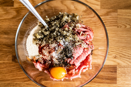 Raw minced meat, egg yolk, onion and seasonings in bowl on wooden background