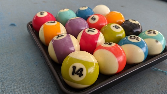 A collection of billiard balls arranged in place. There is ball number 14 which is close to the camera. The ball is on the pool table. There are defects around the ball due to play.