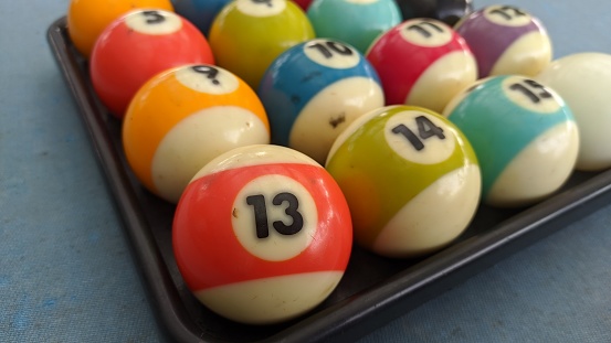 A collection of billiard balls arranged in place. There is ball number 13 which is close to the camera. The ball is on the pool table. There are defects around the ball due to play.