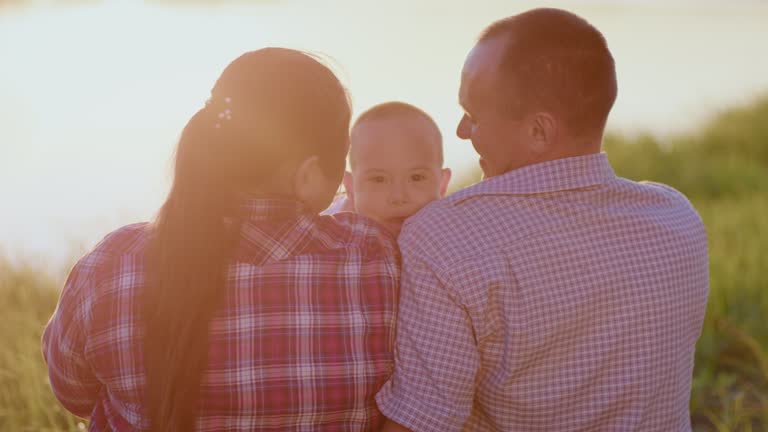 Loving parents hold disabled son on riverbank at twilight