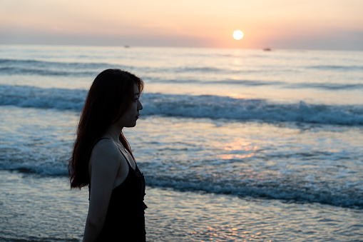 Young Asian woman standing at the seaside watching the sunrise