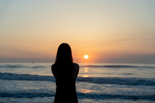 Young Asian woman standing at the seaside watching the sunrise