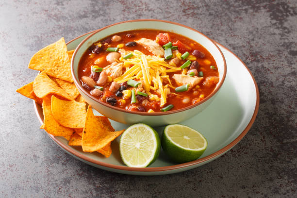 Chicken Taco Soup with black bean, corn kernels, tomatoes topped with cheddar cheese in green bowl, horizontal