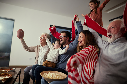 Excited extended family cheering for their favorite sports team while watching a game on TV at home.