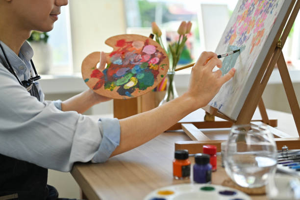 明るいアートスタジオで、パレットを持ち、油絵の具でキャンバスに絵を描くアーティストの手のトリミング画像。 - artists canvas palette paintbrush oil painting ストックフォトと画像
