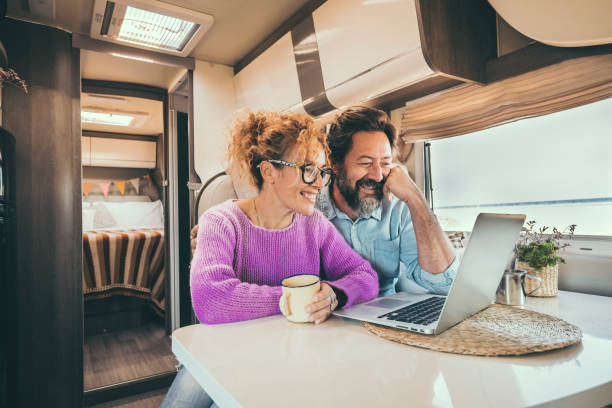 Man and woman using laptop inside camper van during travel lifestyle van life. Happy couple smile in front of a computer during rv motor home vacation. Smart working and digital nomad concept day stock photo