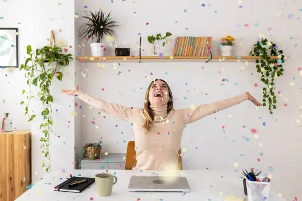 Photo of Young businesswoman celebrating success throwing confetti sitting at home office
