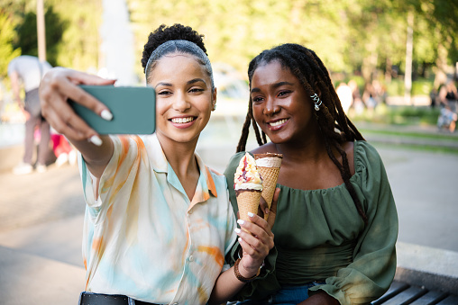 Portrait of the two beautiful girls eating ice cream and taking a selfie outdoors