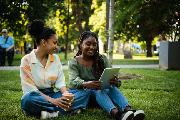 istock Two girls enjoying on the park grass and using tablet 1442151093
