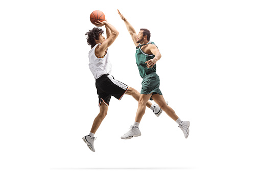 Low angle view of a professional basketball game in 80's. The colors are desaturated. A player failed to block  the opposite team player with a ball. A game is in a indoor floodlit basketball arena. All players are wearing generic unbranded basketball uniform.